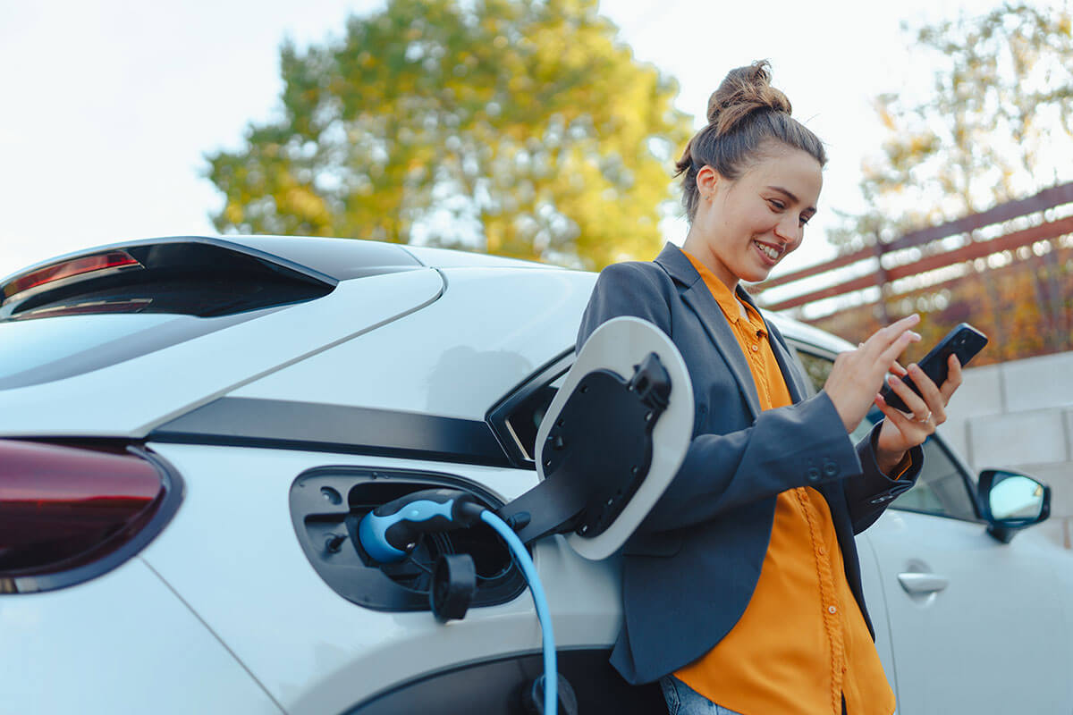 woman with smartphone waiting while her electric car charging in home charging station